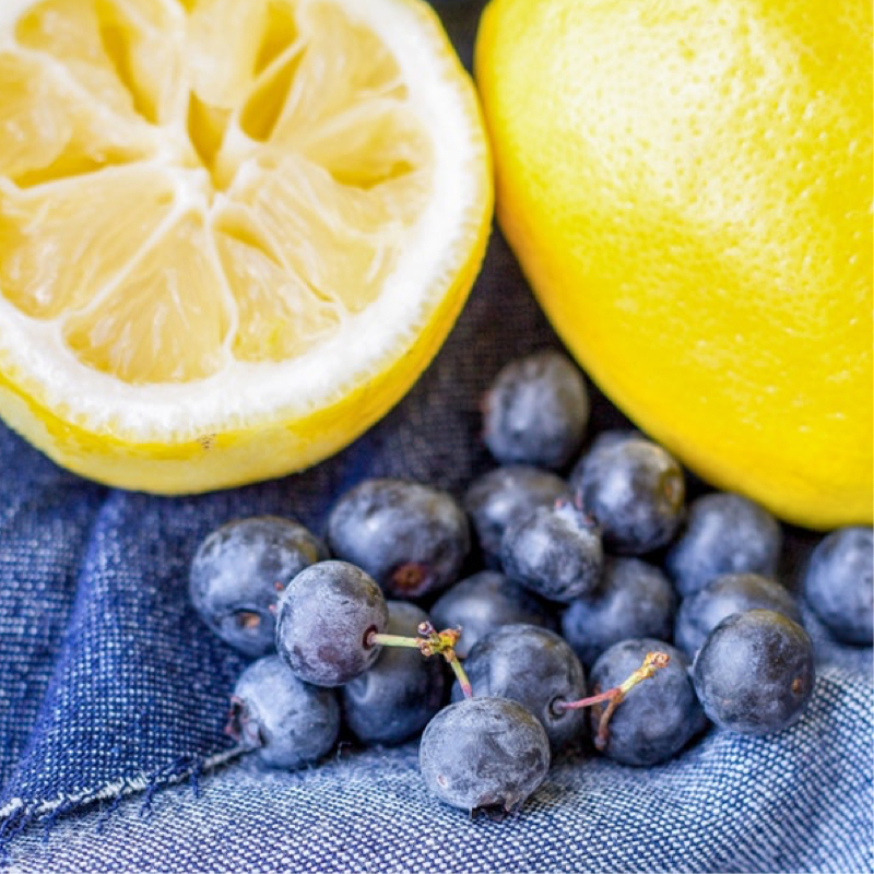 Sliced lemons and blueberries laying over blue fabric.