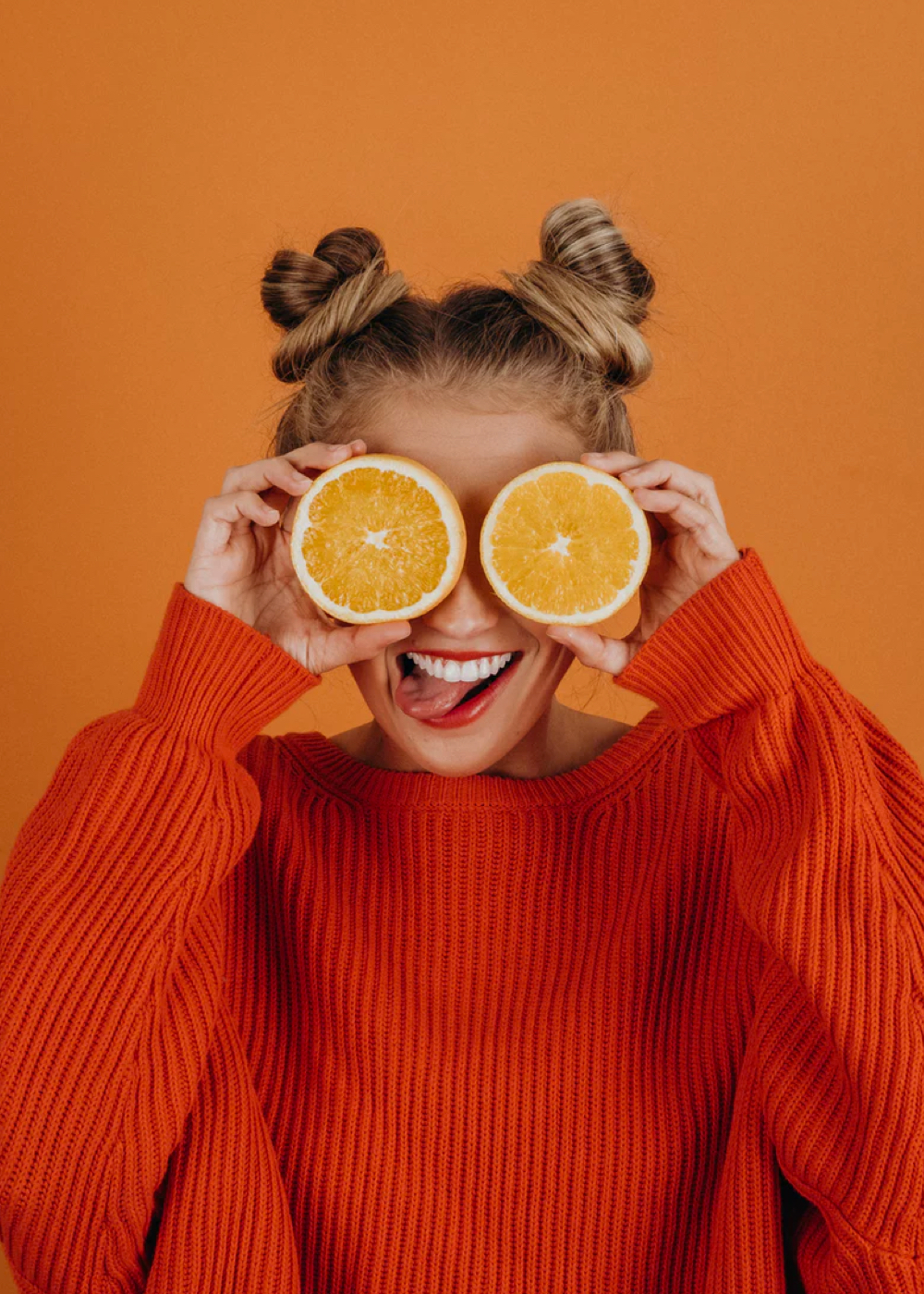 Sophie holding two slices of oranges around her eyes, while smiling with her tongue hanging out.